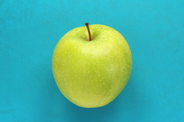 Green yellow apple on a blue background. Juicy ripe beautiful fruit.