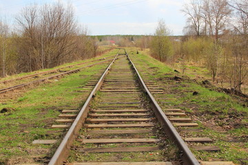 Fototapeta premium The railway stretching into the distance against the background of young green grass and trees in spring.
