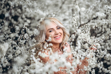 Woman with gorgeous smile, curly blond hair in red dress having fun in blooming garden