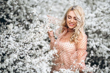 Woman with gorgeous smile, curly blond hair in red dress having fun in blooming garden