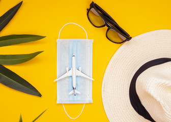 medical mask, sunglasses, hat, plane, palm leaves on yellow background. Concept not flights or travel by covid-19