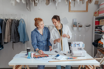 Fashion designer sewing fabrics with assistant. two young designers work in a bright studio, have opened their own business and are ready to take orders. Beginning of work