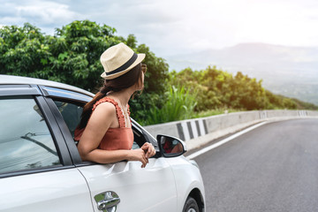Relaxed happy traveler, Young beautiful girl wearing white hat weave Reach out of the car at sunshine and nature view with mountain road background