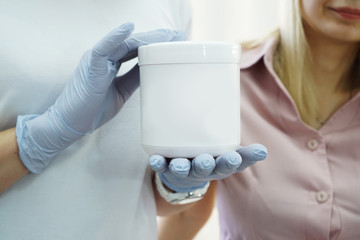 Doctor shows the patient remedy in beauty salon. Cosmetology the doctor advises the patient. Close up photo of white jar with cosmetic