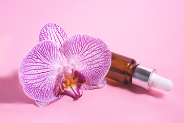 A cosmetic dropper bottle and pink orchid on the pink background.