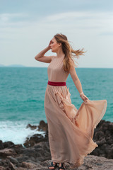 Fototapeta na wymiar beautiful girl in a beige dress stands on a rocky seashore