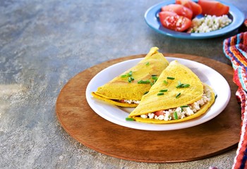 Chilla, tortillas or pancakes made from chickpea flour stuffed with cheese panir and tomato on a white plate on a gray concrete background. Indian food, street food. Vegetarian recipes.