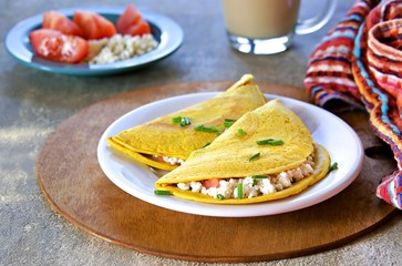 Chilla, tortillas or pancakes made from chickpea flour stuffed with cheese panir and tomato on a white plate on a gray concrete background. Indian food, street food. Vegetarian recipes.