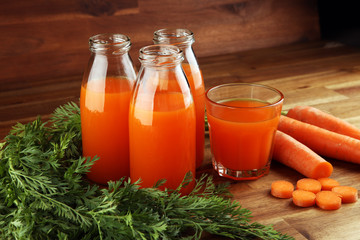 Fresh carrot juice in bottles with organic carrots on table. Vegetable juice set