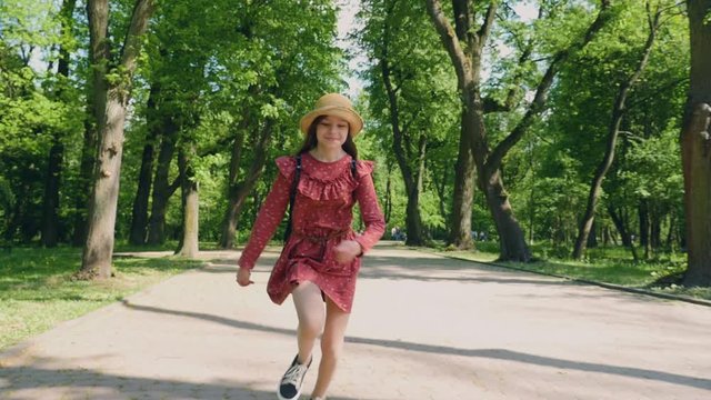 Happy teenage in red dress and hat run and smiling in the park. Slow motion.