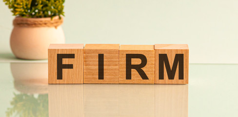 Word FIRM is made of wooden building blocks lying on the table and on a light grey background....