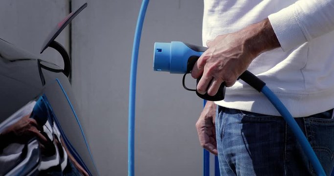 Man opens the socket of his electric black car to connect the recharge plug. Alternative energy with car connected and charging batteries close-up 4K