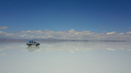 Car in Salar de Uyuni, Salt desert in Bolivia, seen with drone and Andes in the background