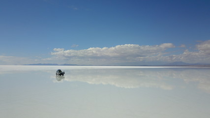 Car in Salar de Uyuni, Salt desert in Bolivia, seen with drone and Andes in the background