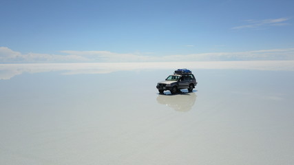 Car in Salar de Uyuni, Salt desert in Bolivia, seen with drone and Andes in the background