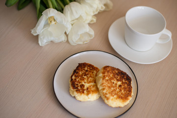 white empty Cup and saucer on the table, white tulips, homemade cheesecakes on a plate (horizontally)