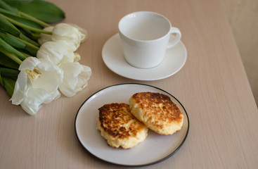 white empty Cup and saucer on the table, white tulips, homemade cheesecakes on a plate