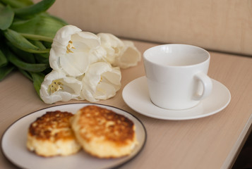 white tulips, homemade cheesecakes on a plate, and a white empty Cup and saucer on the table