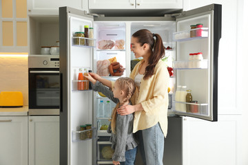 Young mother with daughter taking juice out of refrigerator in kitchen