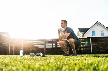 A guy is doing squats in the backyard. Sports training at home, workout outdoors