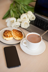 phone, laptop on the table, cup with cacao and saucer on the table, white tulips; morning Breakfast with cacao, Breakfast on a freelance (vertically)