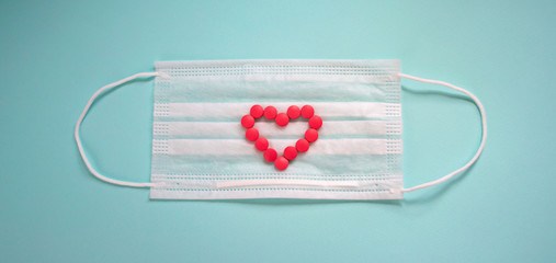Disposable medical face mask and tablets on a blue background. Pink pills in the shape of a heart on a white mask background. Prevention of a pandemic virus.