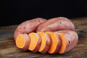 Tree sweet potatoes (batatas), one of which is sliced, on the rustic wooden table with black background. Copy space, space for text