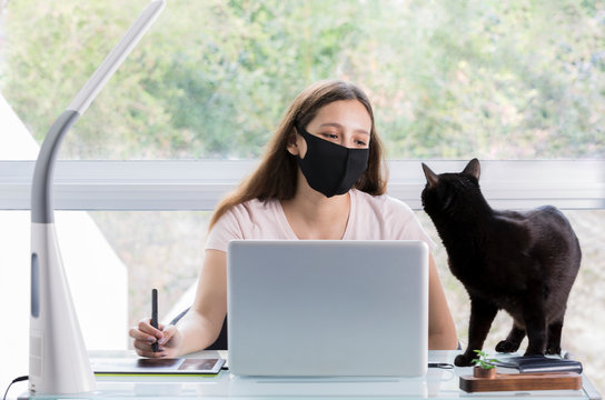 Graphic designer woman working with mouth covers at home and in the company of her beloved cat.