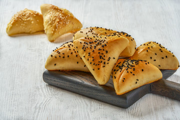 Fatayer pie samosa with white cheese and black sesame seeds on wooden board.