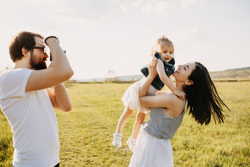 Happy family concept. Father taking photos of mother and little daughter outdoors in a field on summer day.