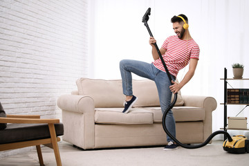 Young man having fun while vacuuming at home