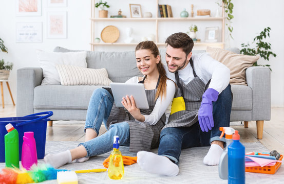 Smiling guy and girl looking at tablet, sitting on living room