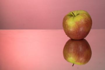 red apple on mirroring table on mirror red background with reflection isolated close up