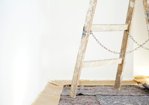 Real old wooden ladder of a painter in use for an interior renovation. Painter cover fleece for protection of floor surfaces. stepladder with chains and paint splashes.