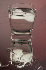 Bartender pouring up frozen vodka from a bottle into two shots glasses with ice cubes against black background. Barman pour of clear transparent alcohol drink rum tequila in shot-glass