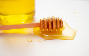 glass jar with honey and with a wooden honey stick on a white background.