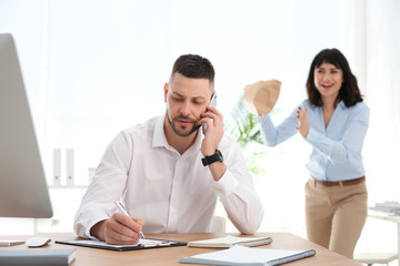 Young woman popping paper bag behind her colleague in office. April fool's day