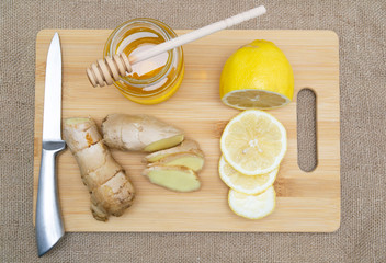 sliced slices of ginger lemon and honey on a wooden board on a sackcloth background. top view.