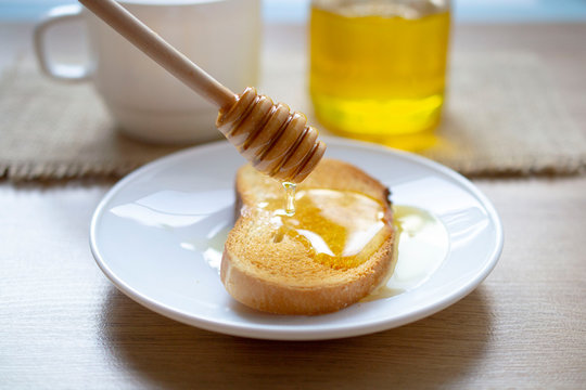 honey dripping from a honey stick on a toaster. background cup with a glass jar of honey