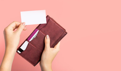 Female hand holds a burgundy leather purse with credit cards and takes out a blank business card on...