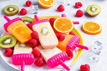 Summer refreshing homemade popsicles with oranges and kiwi. Healthy snack with fruits and frozen juice for summer heat on concrete table top, flat lay, copy space