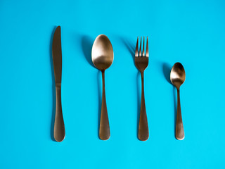 set of tableware. Knife fork spoon made of yellow metal imitating gold on a blue background