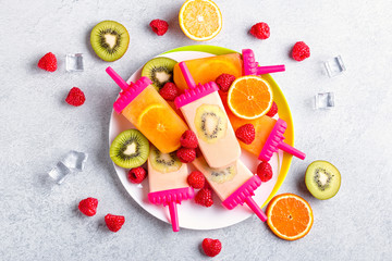 Summer refreshing homemade popsicles with oranges and kiwi. Healthy snack with fruits and frozen juice for summer heat on concrete table top, flat lay, copy space