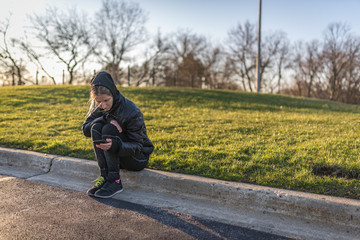 Fototapeta premium Portrait of a girl, sitting on a curb, looking at her smartphone
