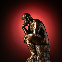 A bronze replica statue of Rodin's Thinker on a red background with vignette