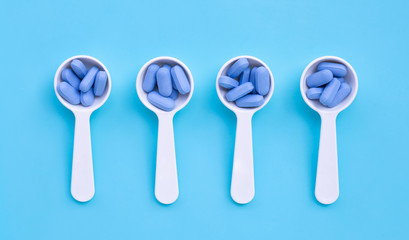 Medical blue pills with white plastic spoon on blue background.