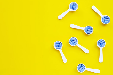 Medical blue pills with white plastic spoon on yellow background.