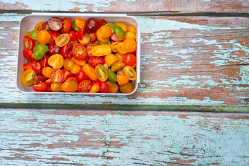 Colorful mix of cherry and grape tomatoes, sliced in half and placed in white plastic mixing bowl, on a wooden background.