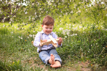 Little cute blond boy playing with a wooden plane in the summer park on the grass on a sunny day