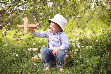 Little cute blond boy playing with a wooden plane in the summer park on the grass on a sunny day